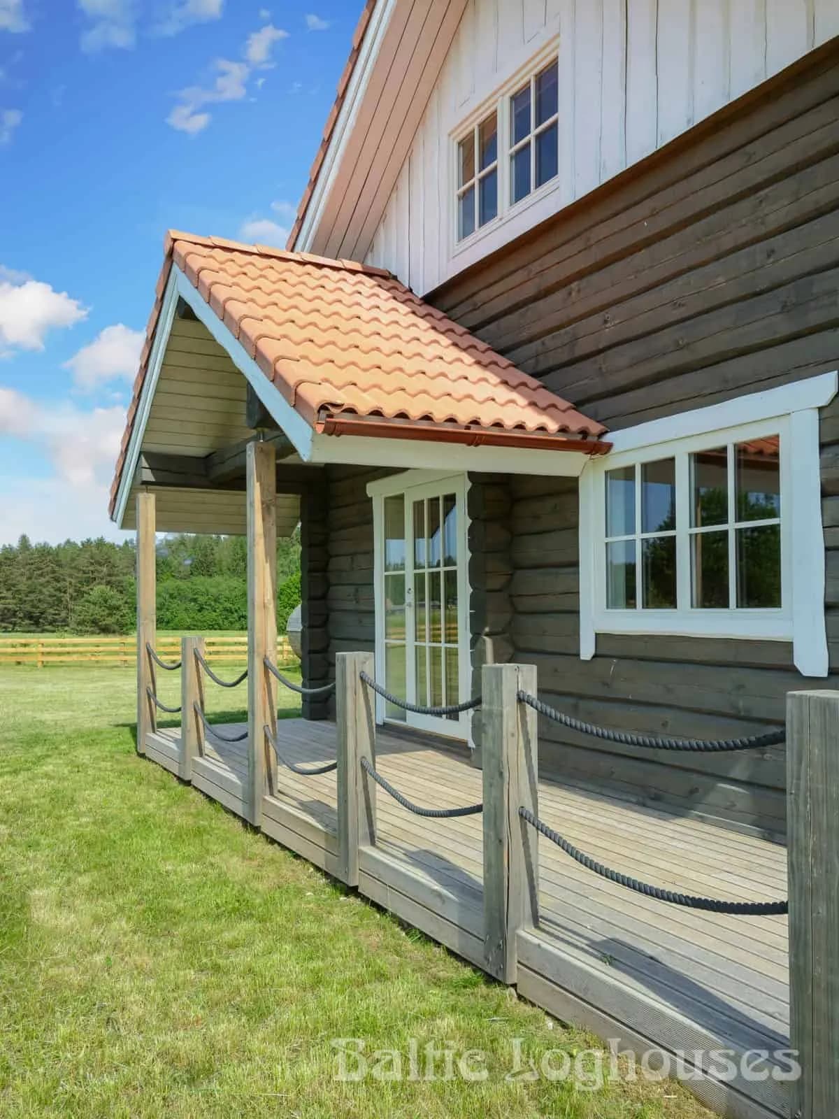 Kaetud puitterrass punase kivikatuse ja nööripiirdega Kiidjärve palkmajal, taamal mets. Töö tegi Baltic Loghouses.