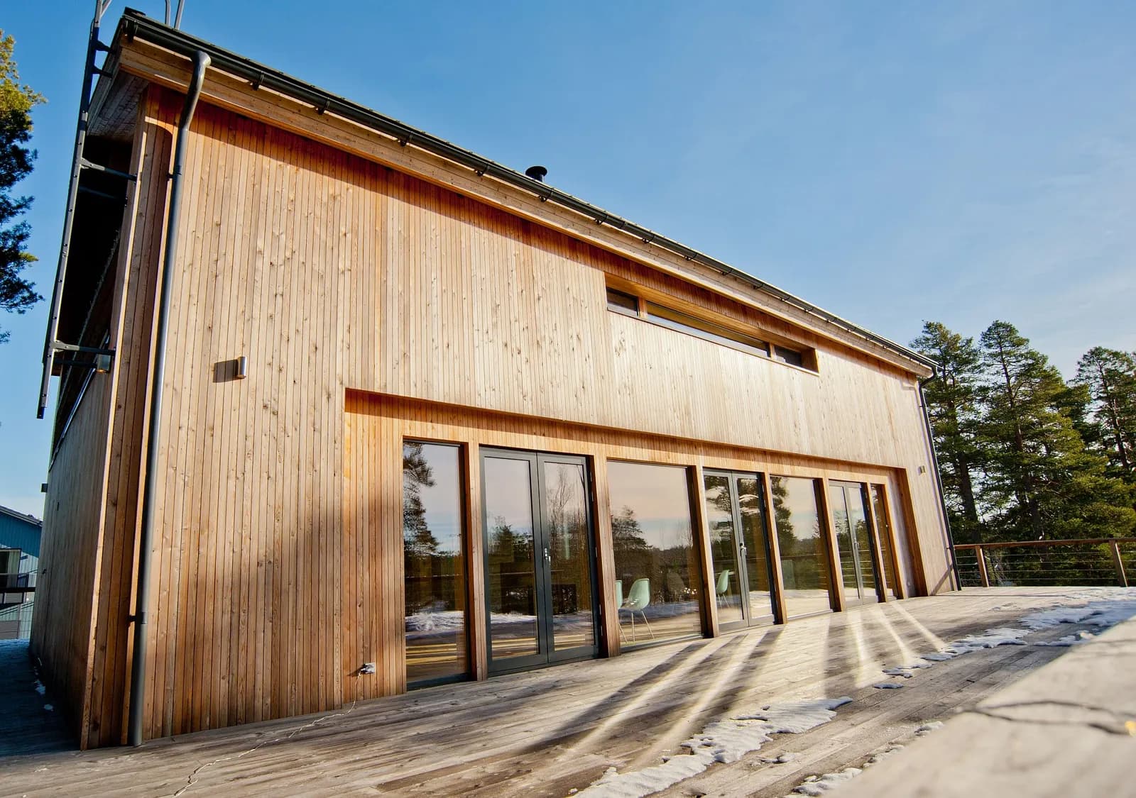 Lumise krundiga välisvaade, lehisevoodriga viil ja põrandast laeni klaasitud nurk, minimalistlik põhjamaine arhitektuur. Töö tegi Hobbiton.