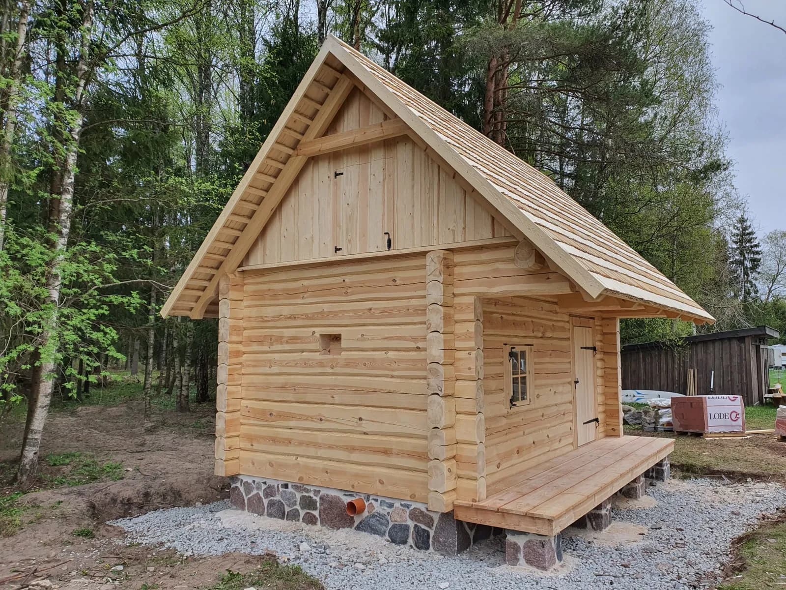 Loodusliku viimistlusega saunahoone välisvaade teisest nurgast, kevad-suvine roheline taust. Töö tegi Hobbiton.
