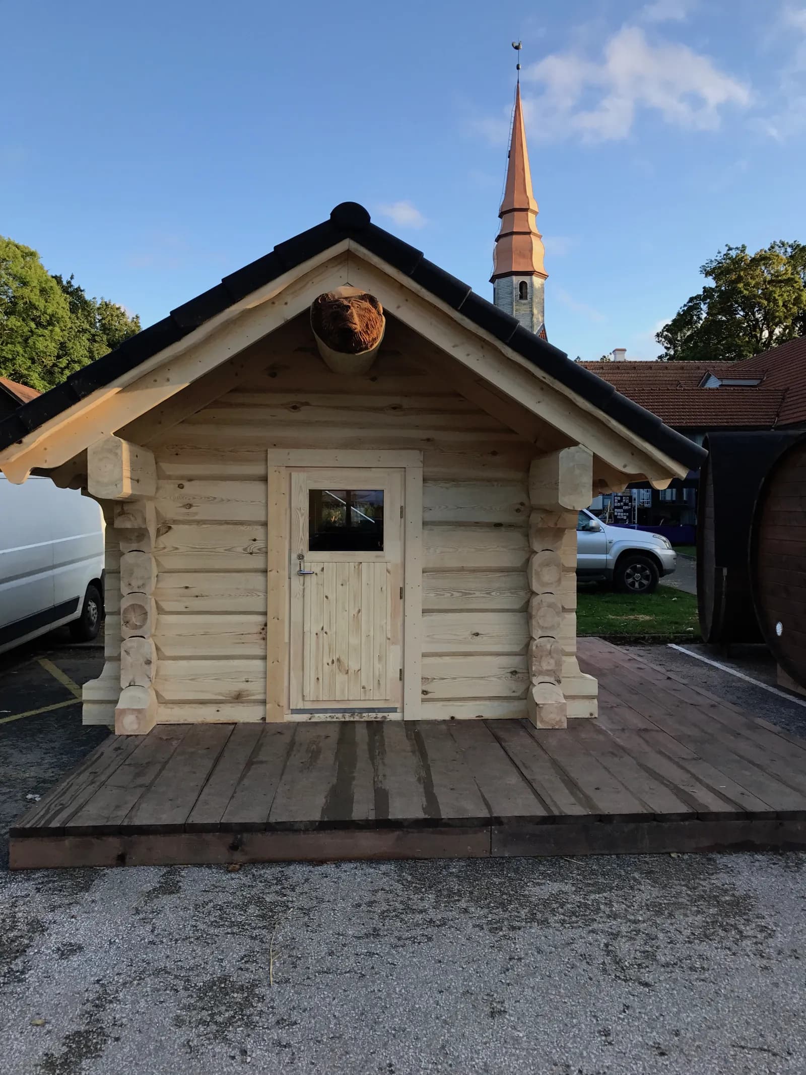 Töötlemata palgist aiasaun musta plaatkatuse ja nikerdatud karupea viiluehisega. Töö tegi L.L. House.