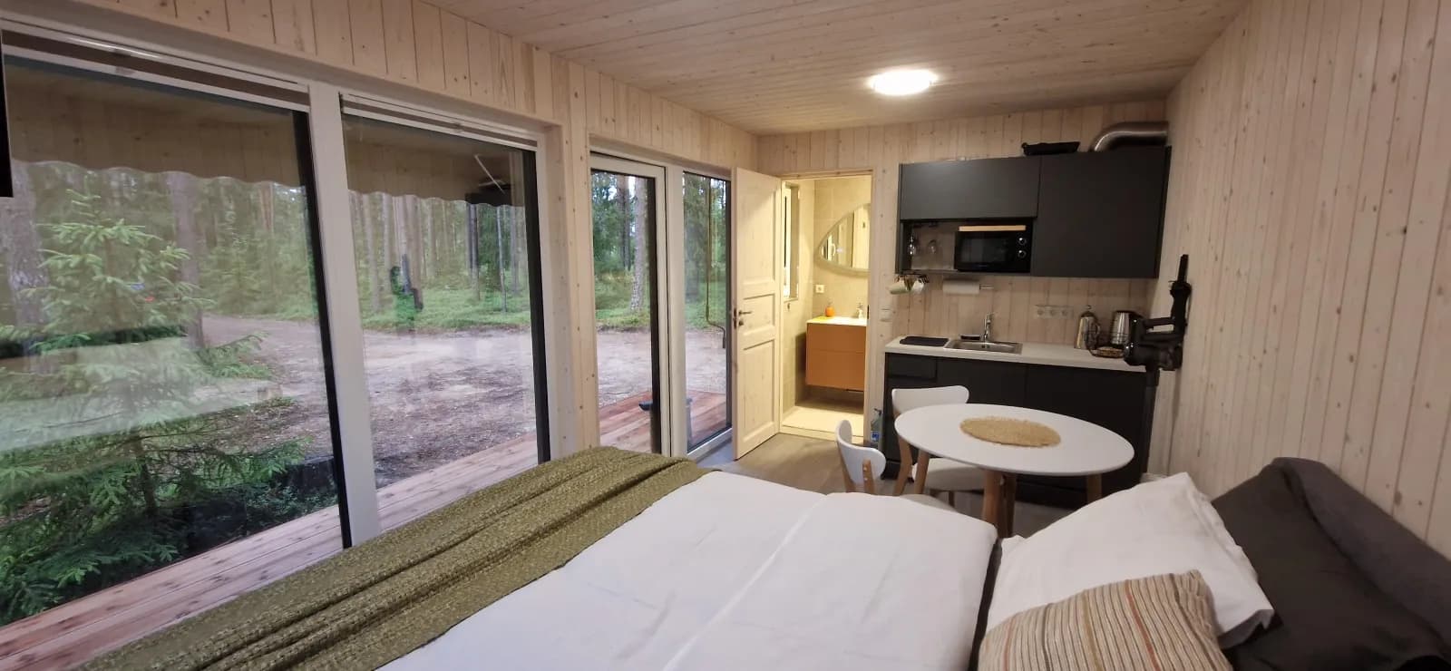 Klaasidega moodulmaja interjöör, avatud planeering koos voodi, köögisopi ja söögilauaga. Töö tegi L.L. House.