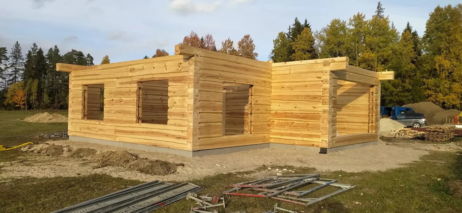 Palkmaja seinad valmis nurgaliidetega, ilma katuseta, raudbetoonvundament nähtaval, sügiseses lehestikus, autod platsi ääres. Töö tegi Palkehitus.
