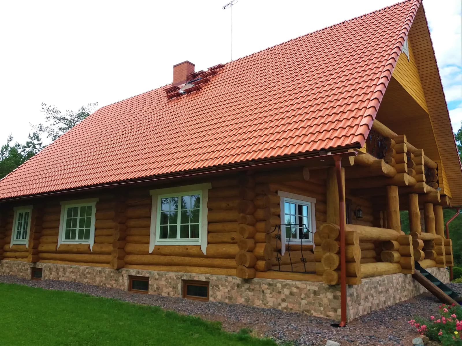 Ühekorruseline ümarpalkmaja eestvaade, punase katusekivikatuse ja valgete akna-/ukseraamidega, kiviplindril, muruplatsil. Töö tegi Palkmaja Ehitus.