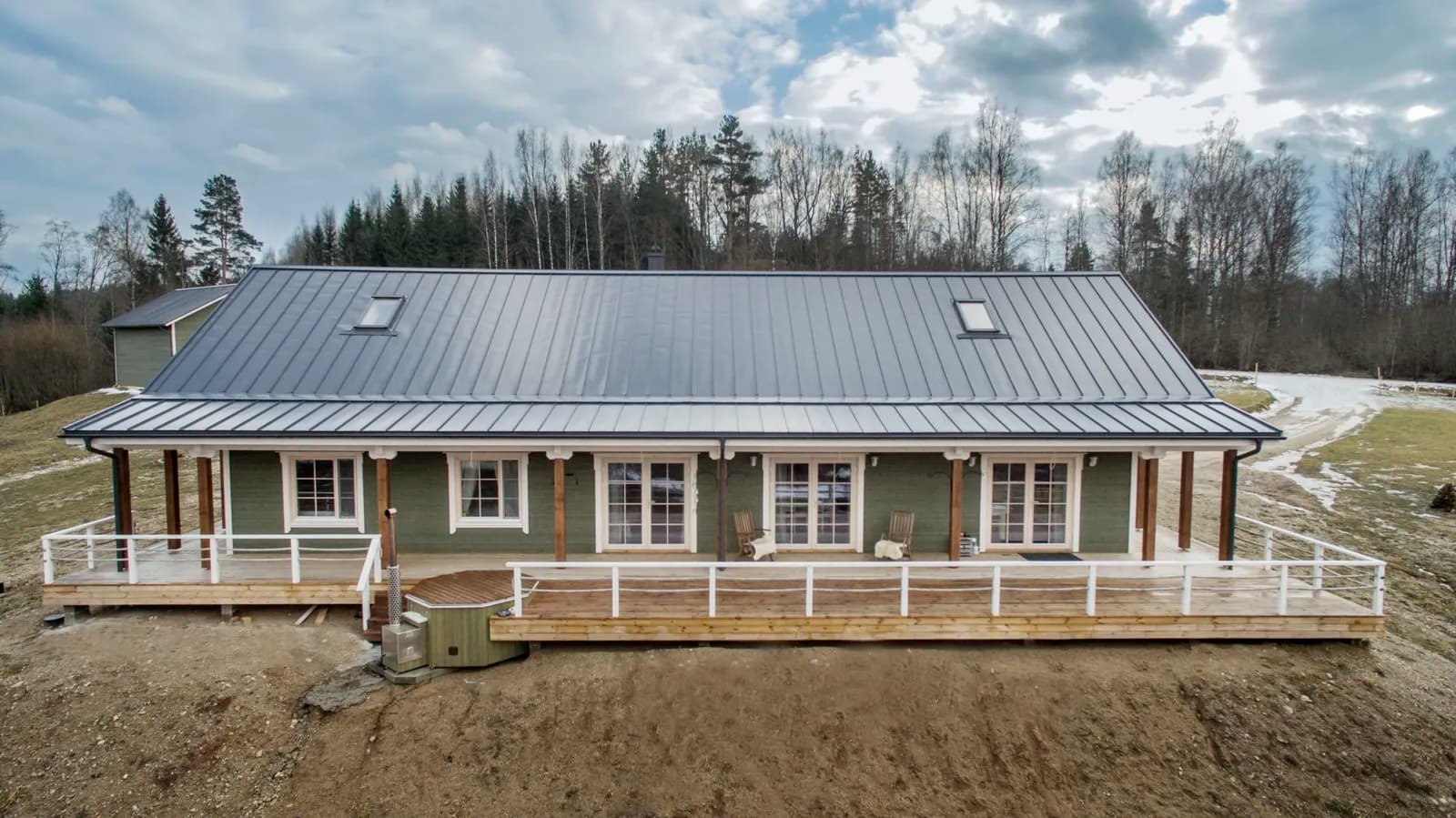 Õhufoto pikast ühekorruselisest rohelisest palkmajast varikatusega veranda ja metsatagustega. Töö tegi Ritsu.