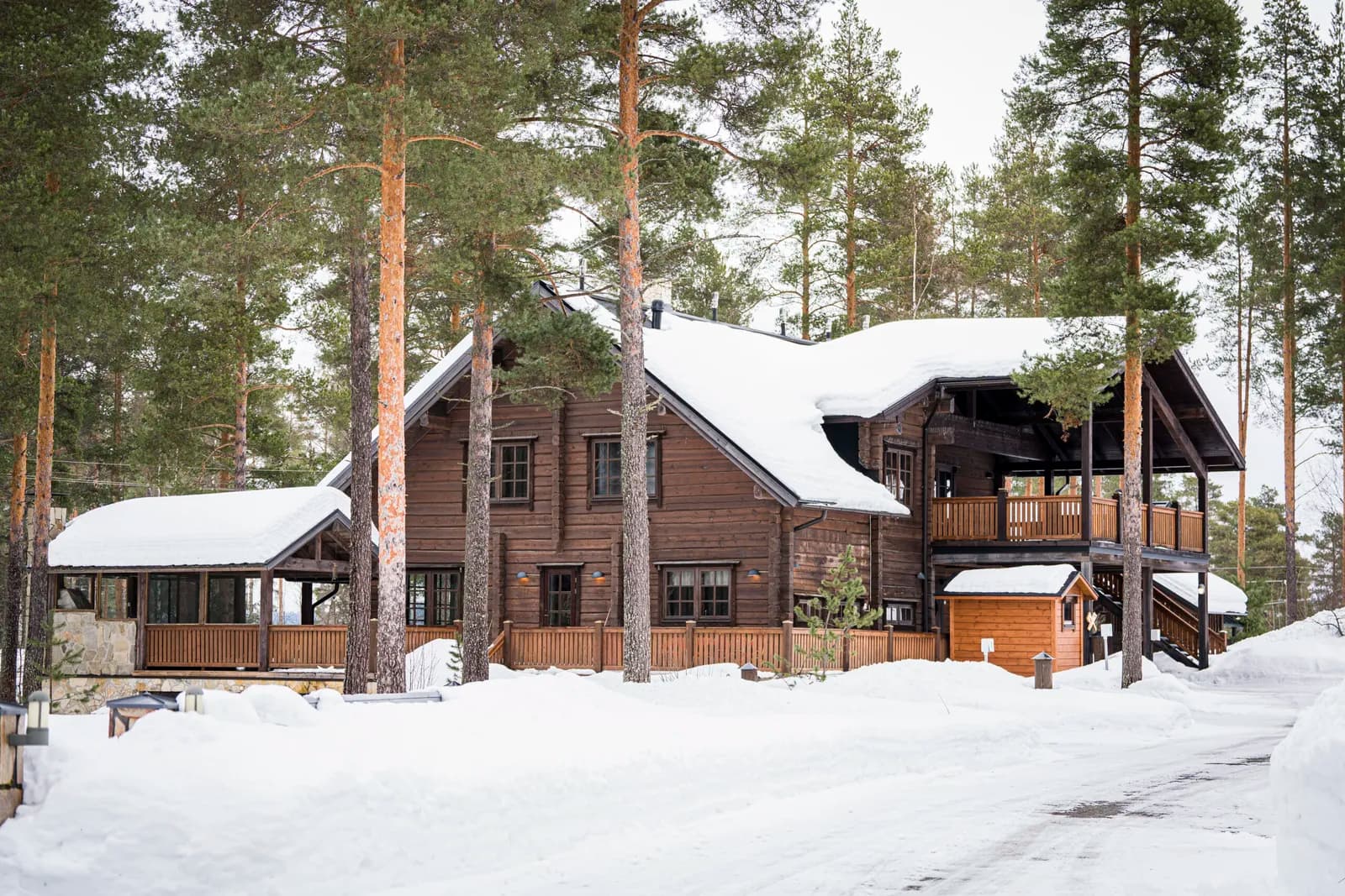 Mitmest omavahel seotud tumedast palkhoonest koosnev hoonestik sügavas lumes, mitmel tasapinnal katused ja rõdu, päevavalgel. Töö tegi Eesti Käsitöö Palkmajad.